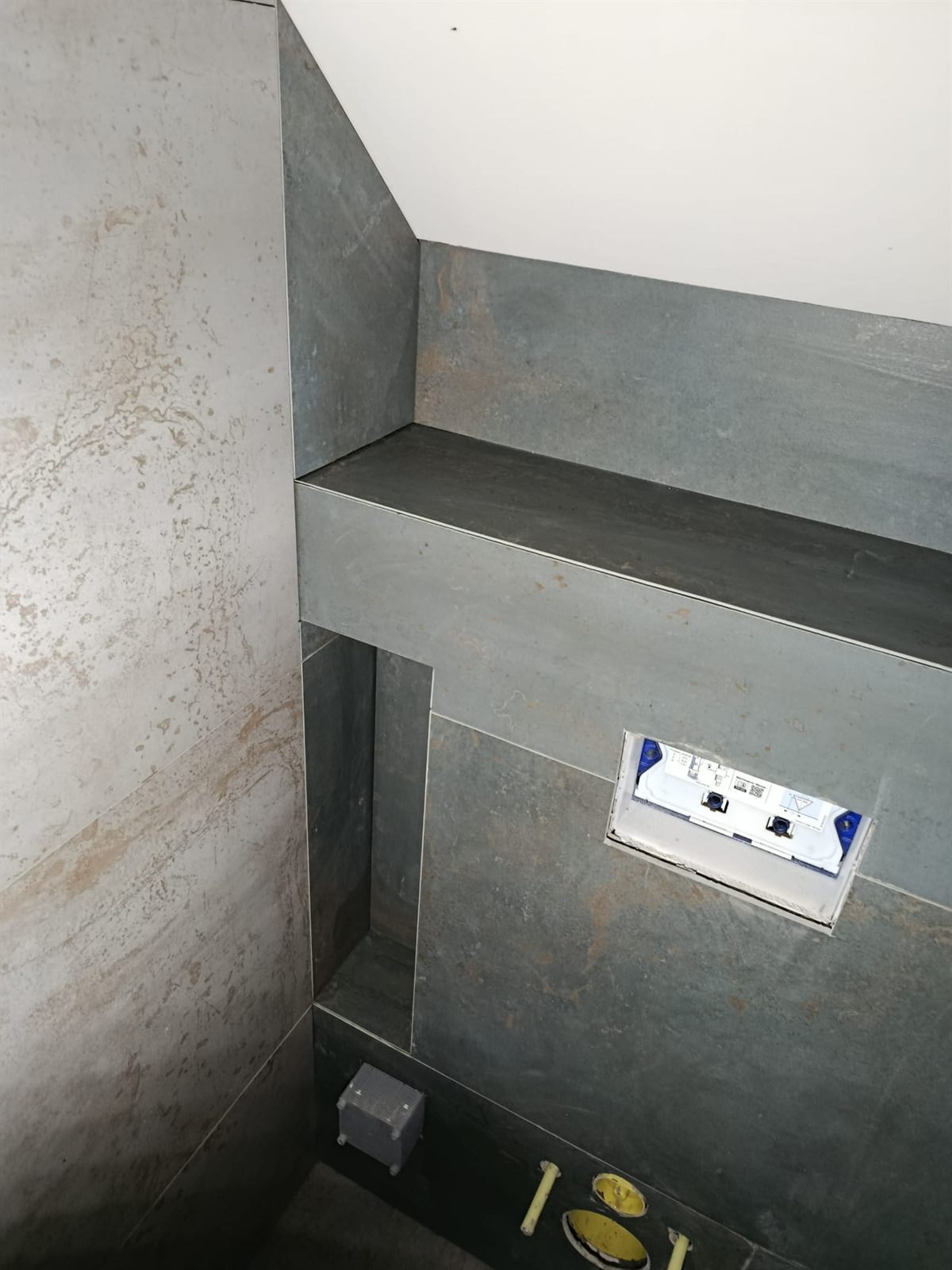 Roh WC s šedým obkladem a modulem splachování